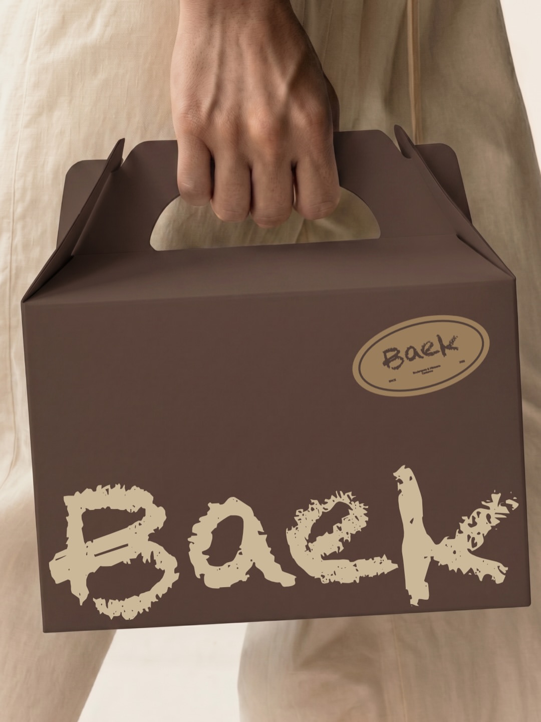 Une boîte à gâteau brune au lettrage Baek, portée à la main.